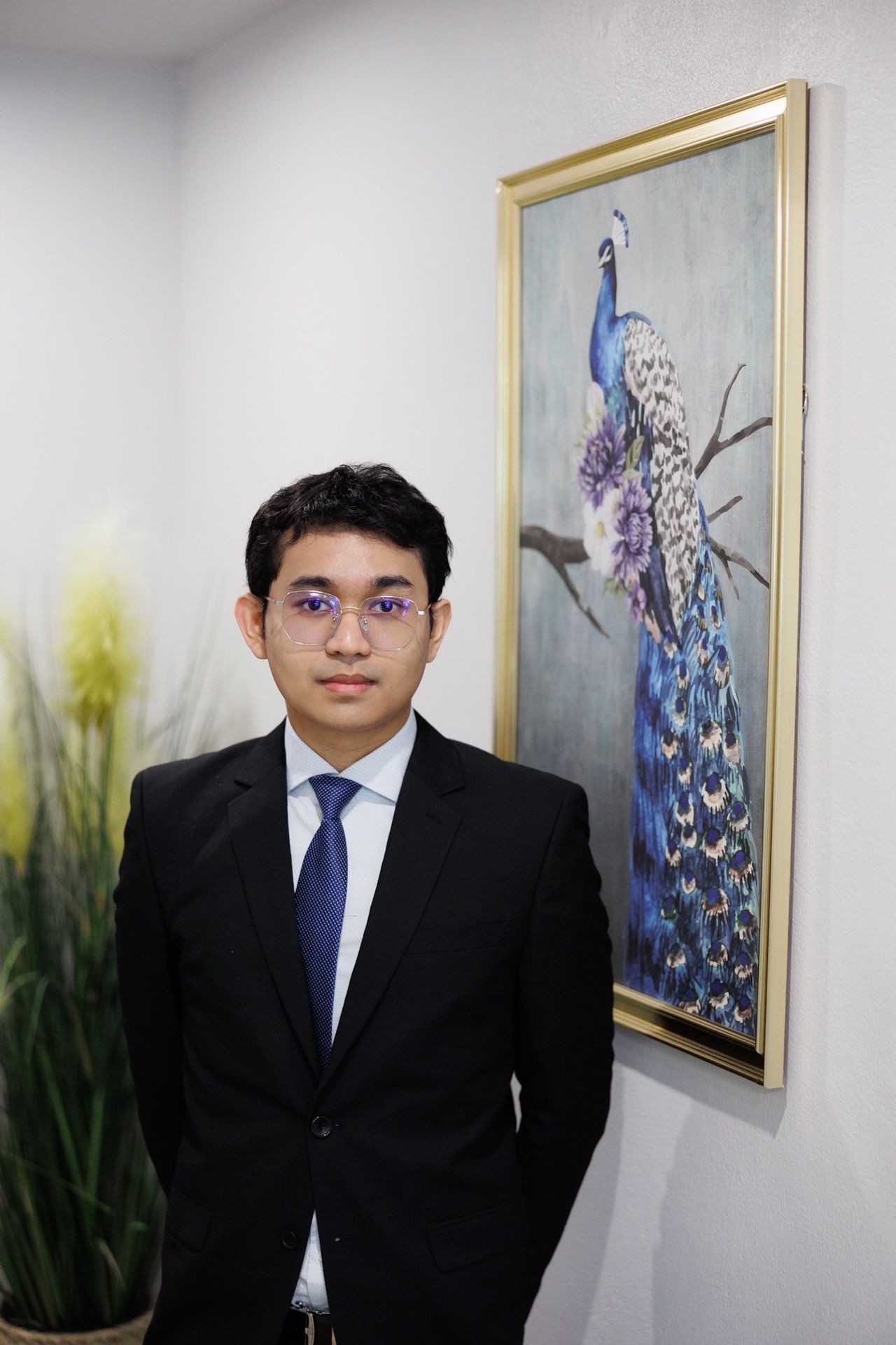 consultant in a suit standing next to a framed peacock painting on the wall.